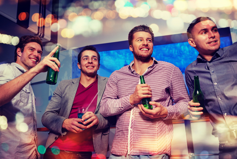nightlife, party, friendship, leisure and people concept - group of smiling male friends with beer bottles drinking and pointing finger to something at nightclub